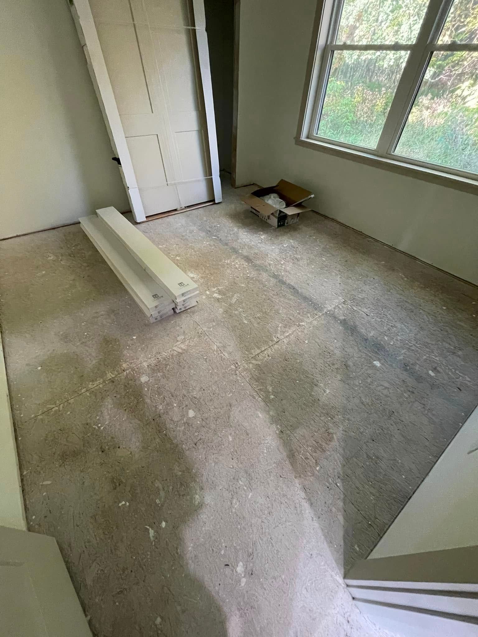 Empty room with concrete floor, doorway, window, and discarded building materials.