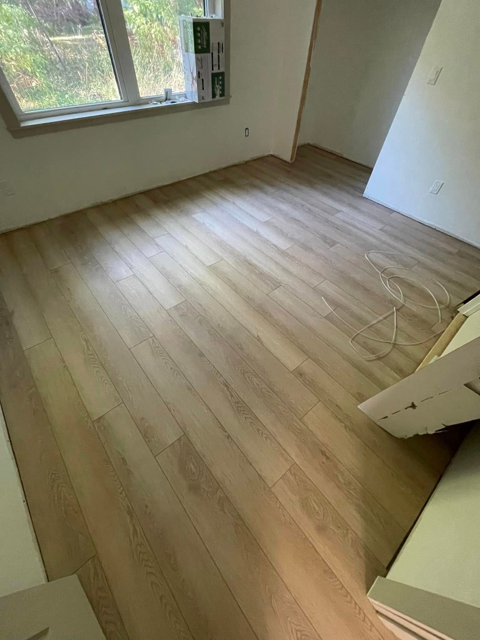 Empty room with light-colored wood flooring, natural light through a window, and unfinished walls.