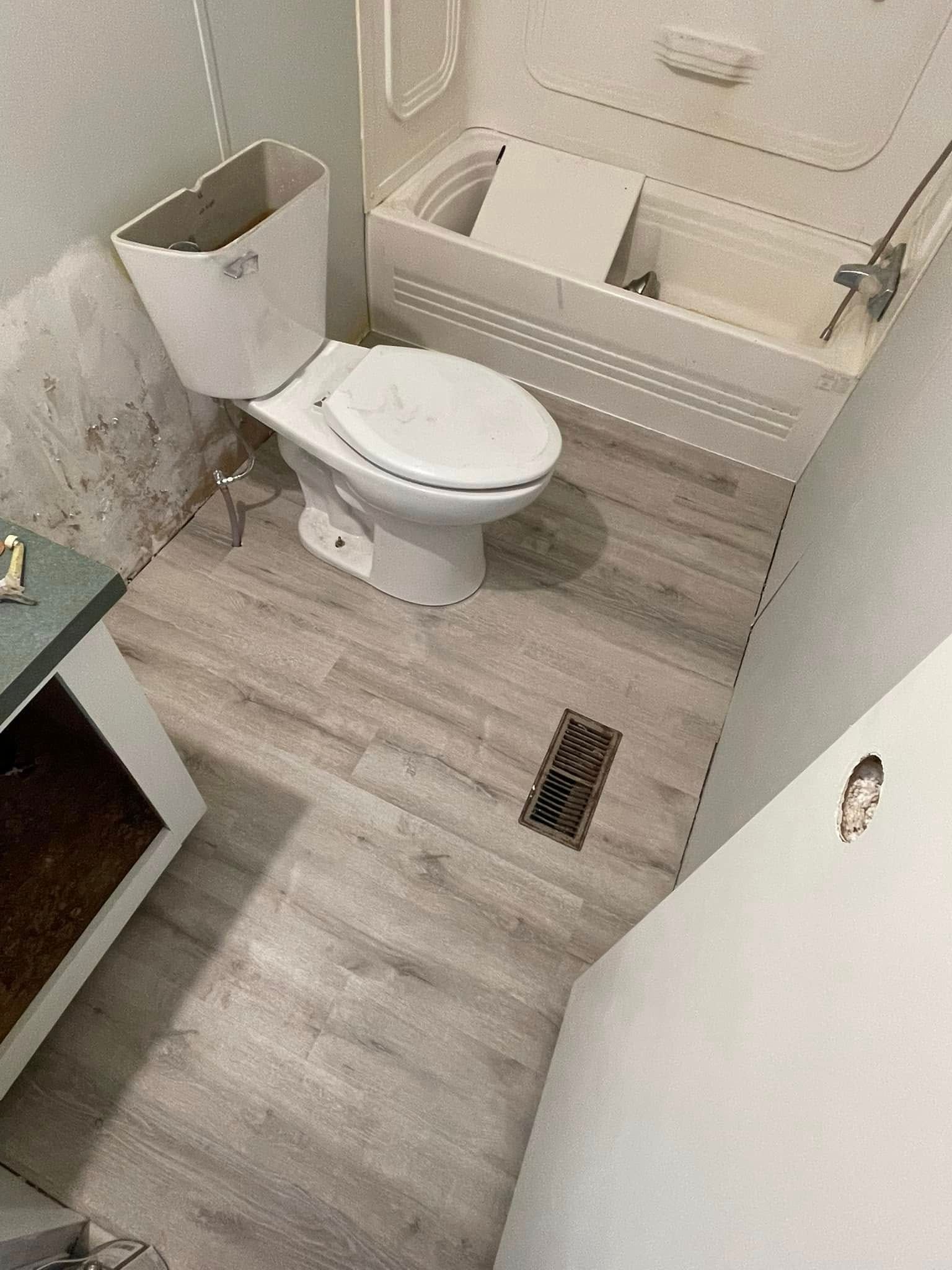 Bathroom with toilet, tub, and new flooring; the wall has potential mold.