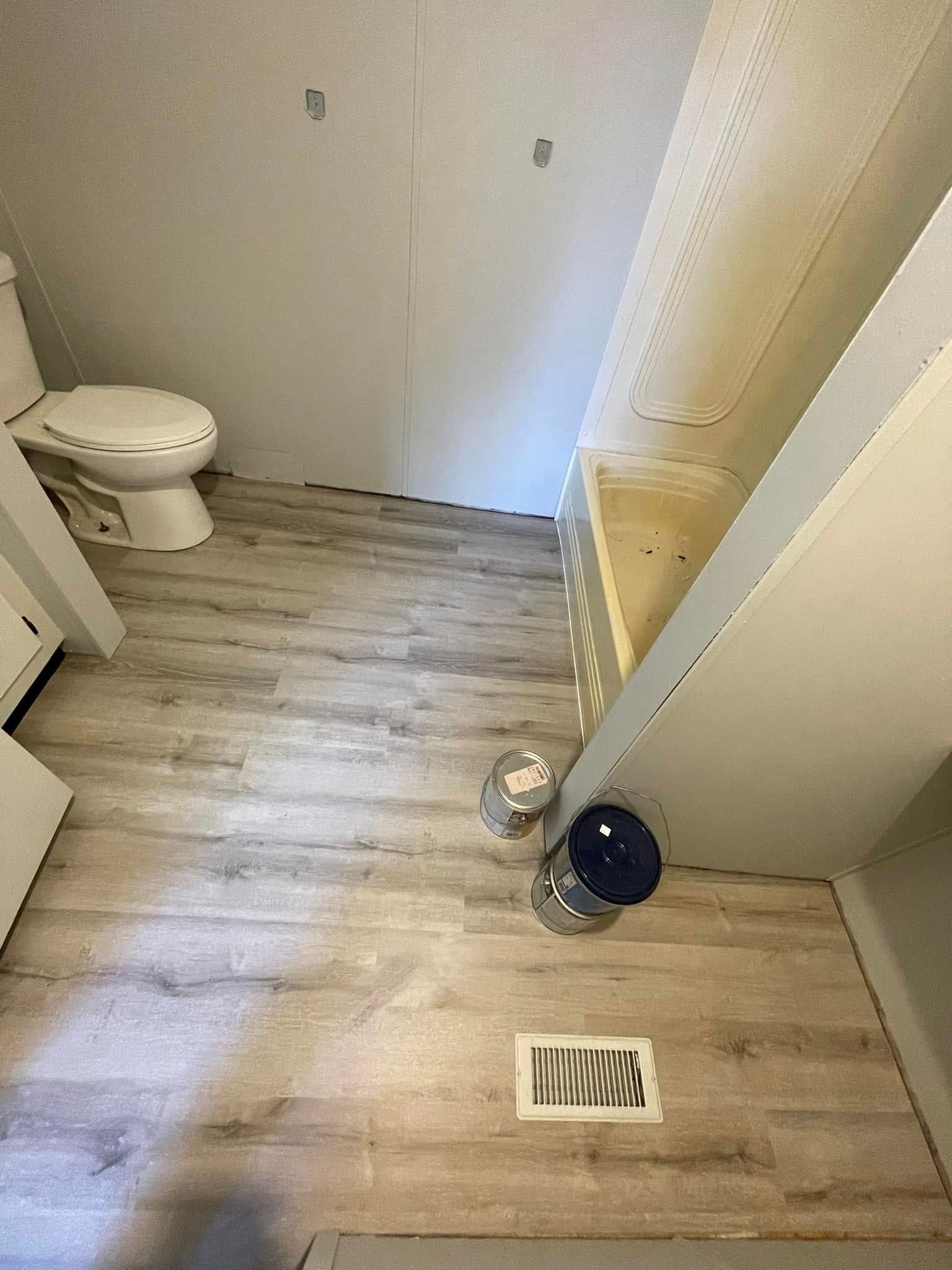 Bathroom with toilet, flooring, and air vent. Two paint cans are on the floor near the steps.
