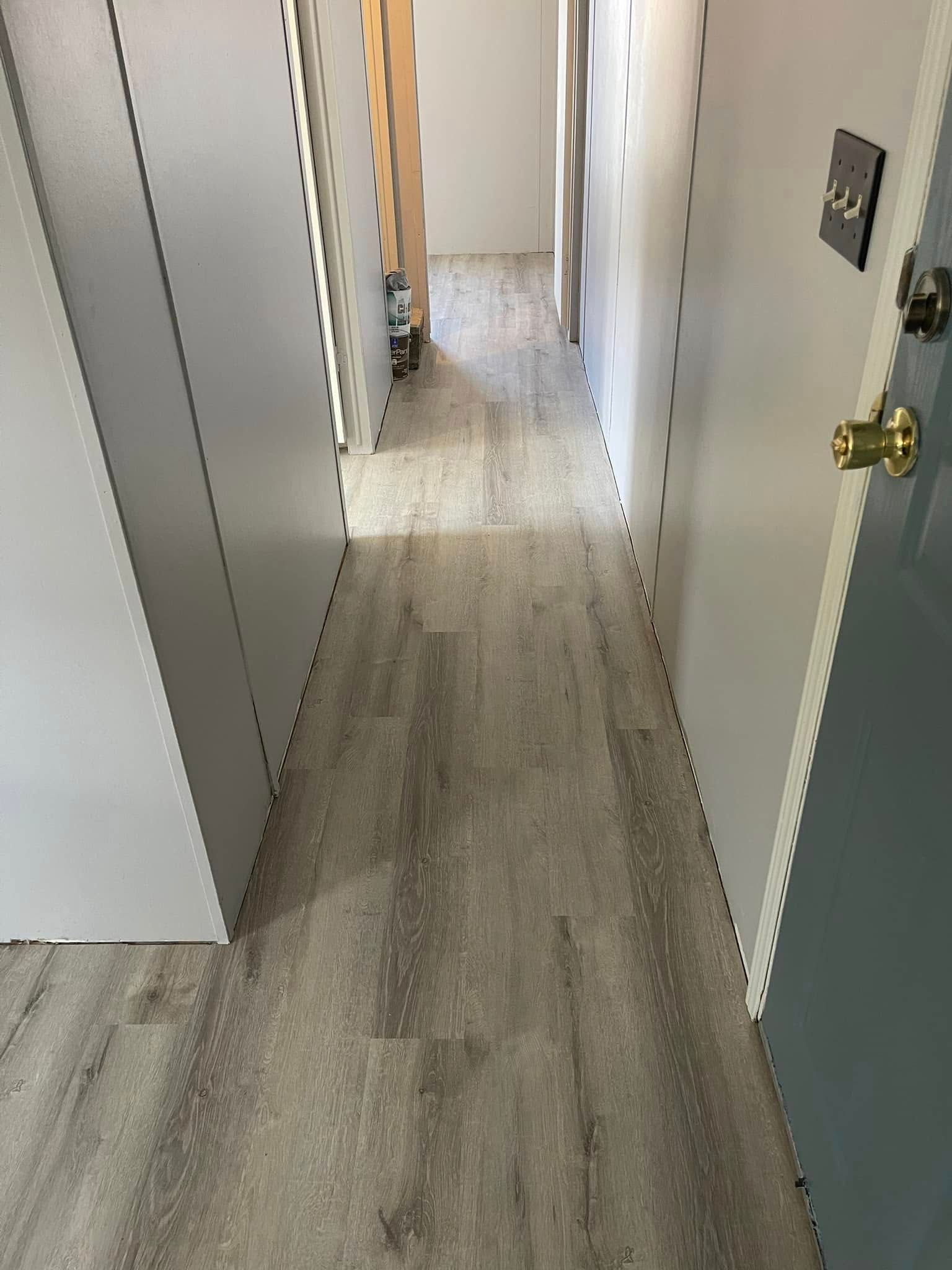 Narrow hallway with wood-look flooring, bordered by white and gray doors.