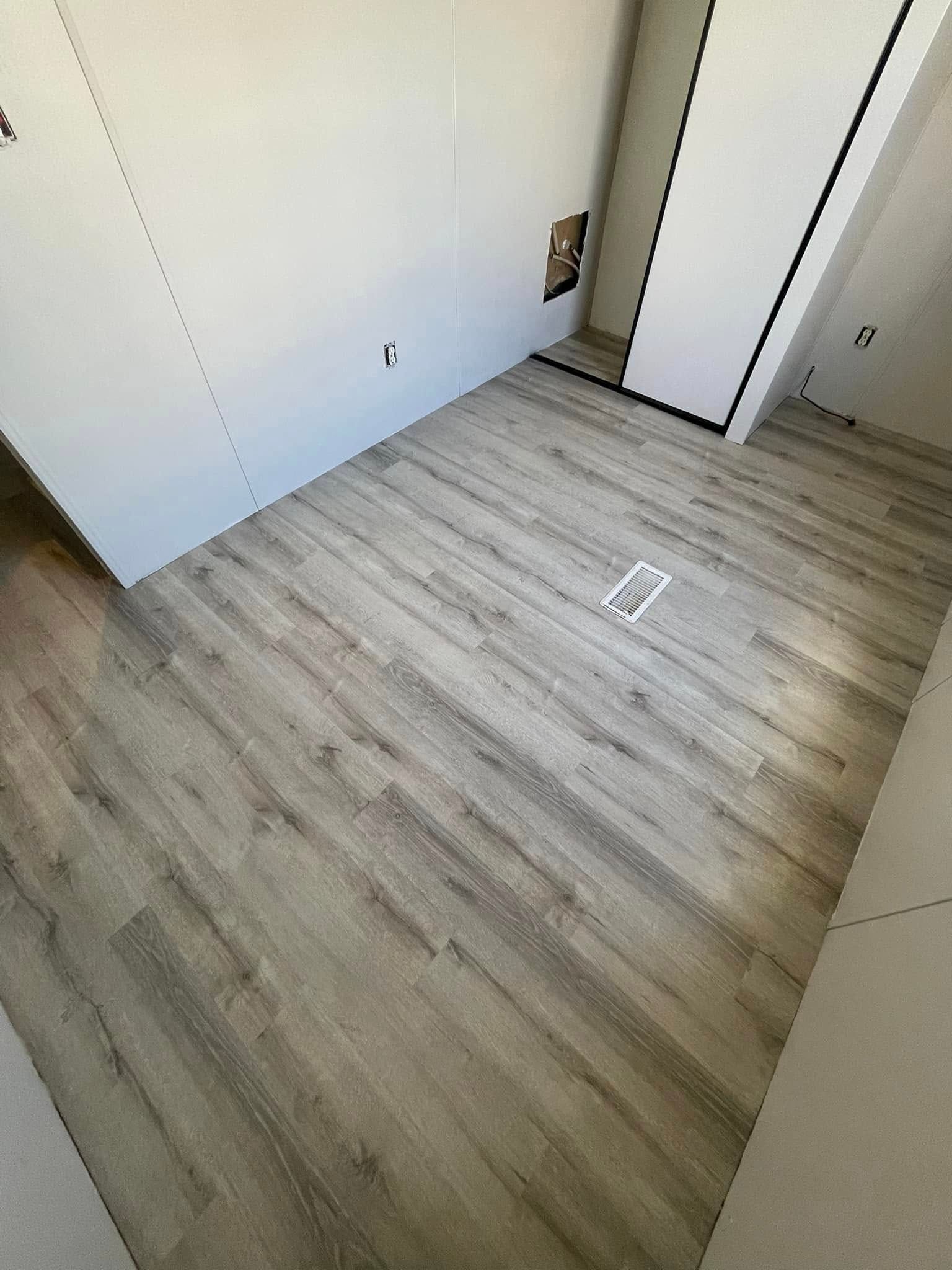 Room with gray wood-look flooring. White walls with a doorway and a vent in the floor.