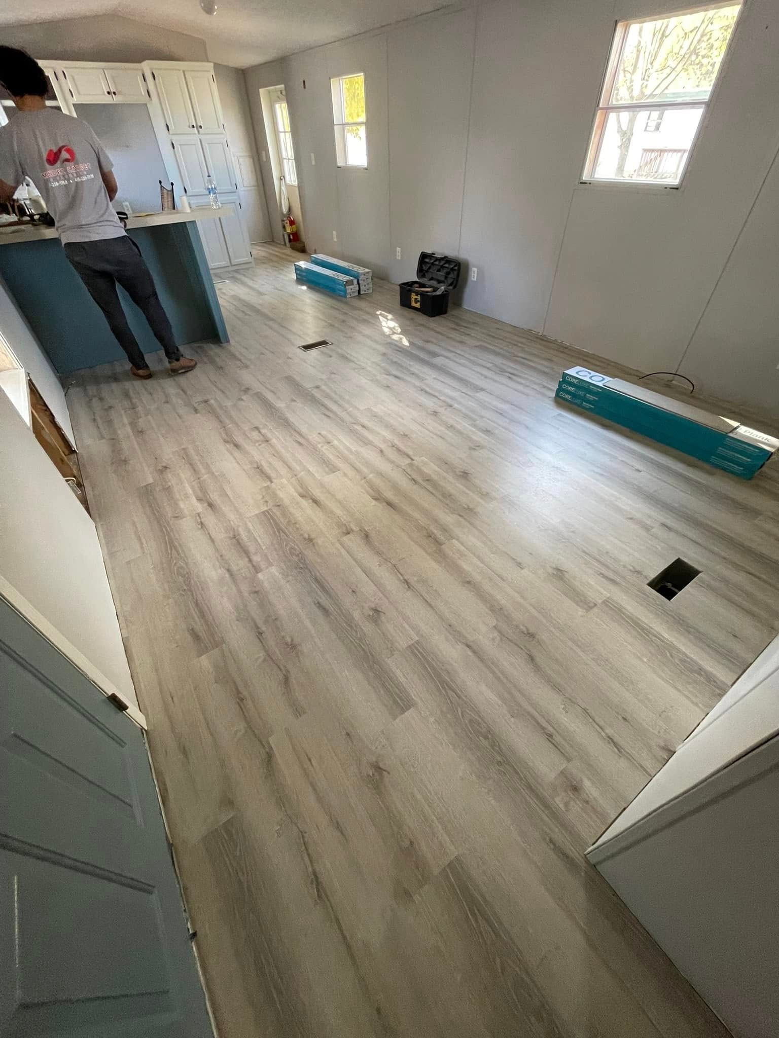 Interior with new light gray wood-look flooring and teal accents. Two people working, rolls of flooring visible.