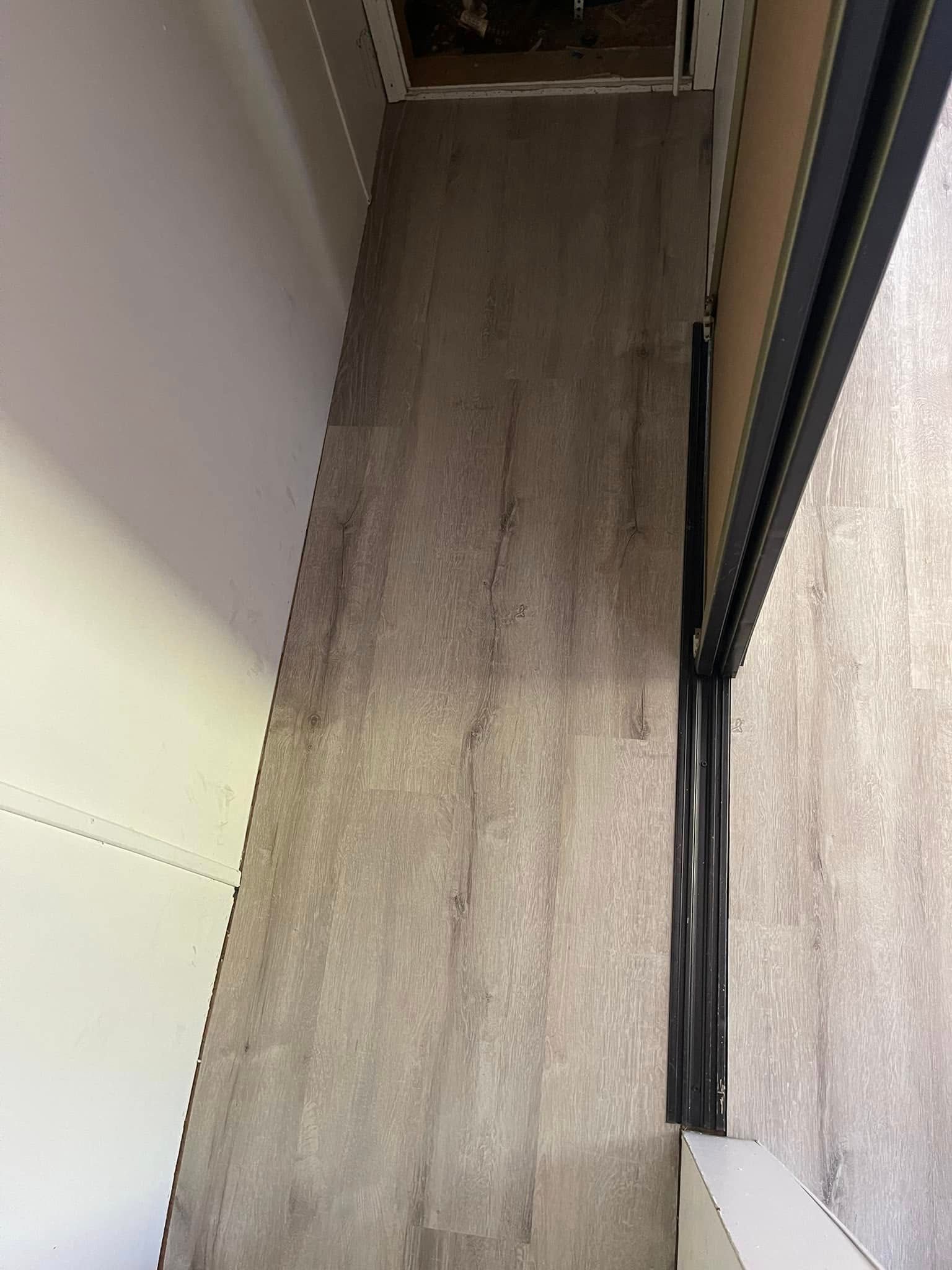 Narrow hallway with wood-look flooring next to a sliding glass door. A white wall is on the left.