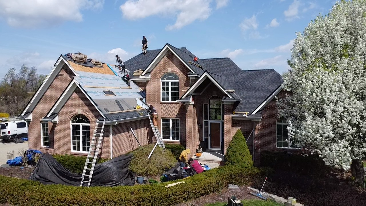 A group of people are working on the roof of a large brick house. A group of people are working on the roof of a large brick house.