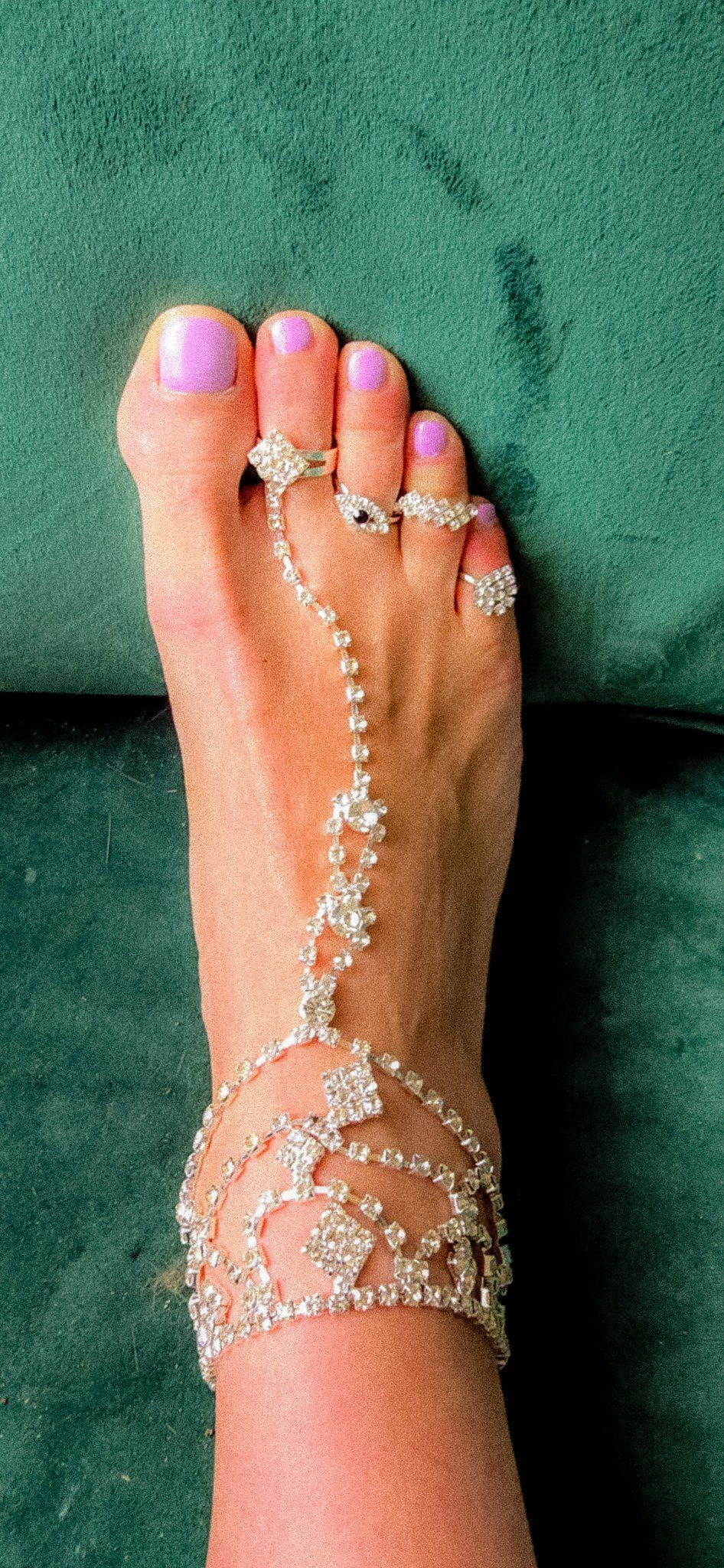 Blote voeten met donkere nagellak op een zandstrand, met een enkelbandje om.