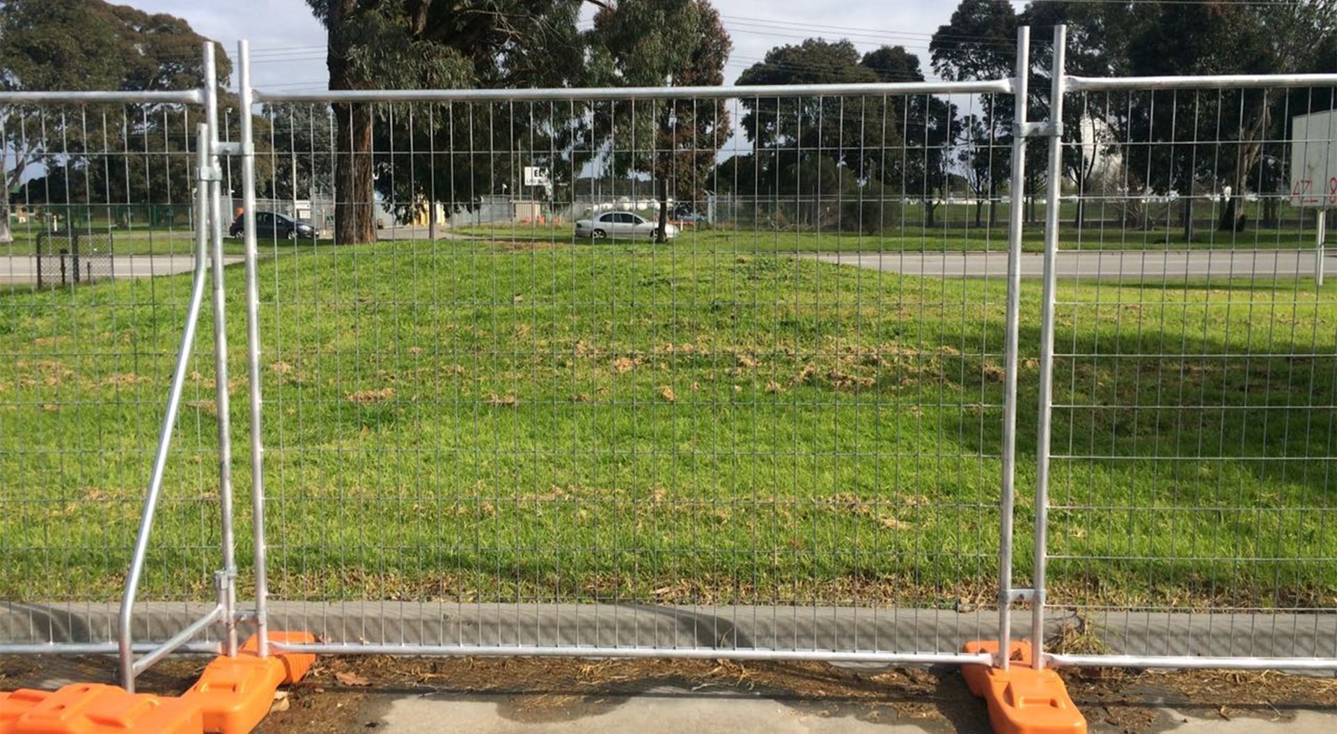A temporary metal barrier fence securing a construction site with orange safety markings.