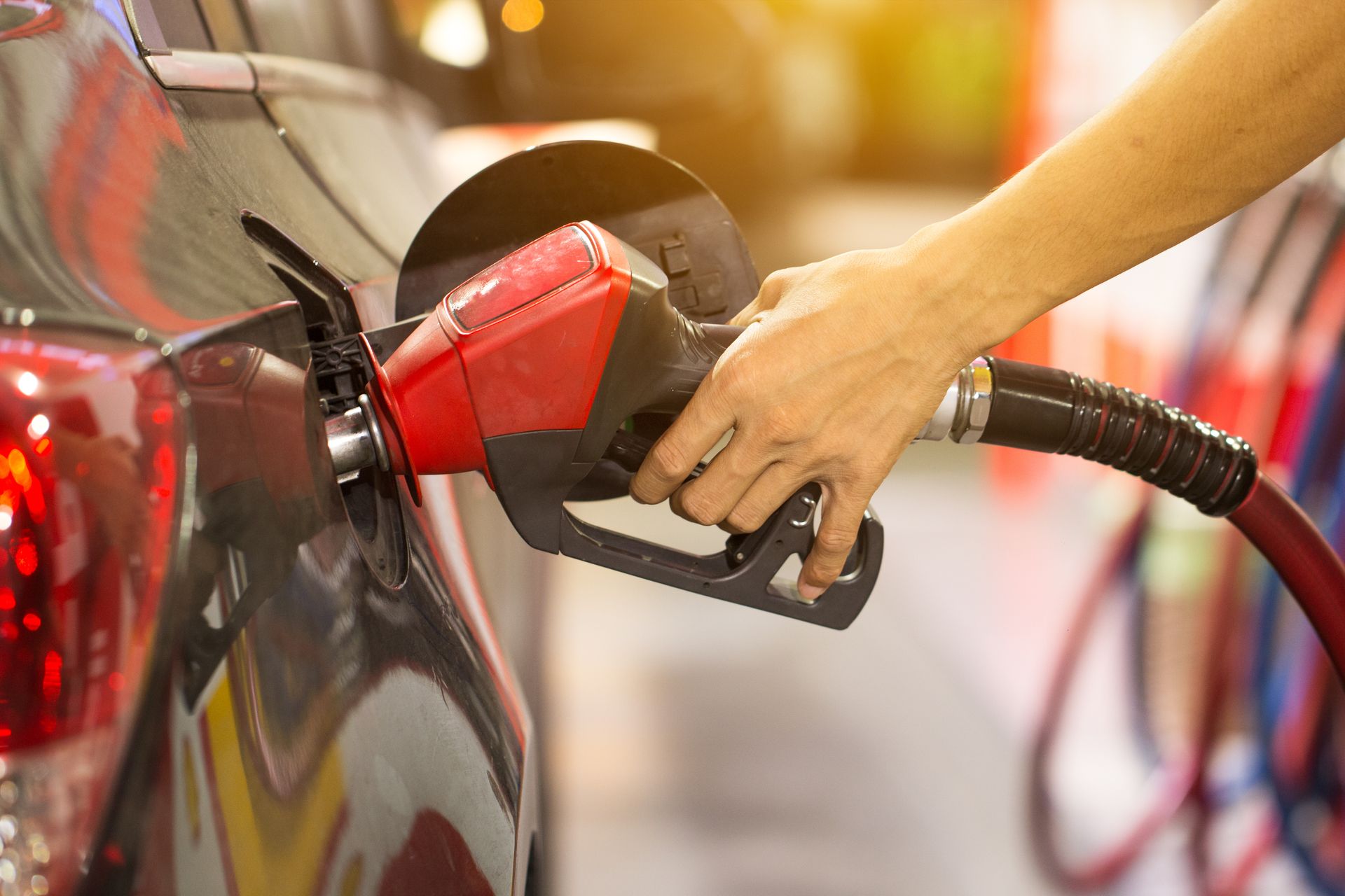A close-up view of a hand inserting a red fuel nozzle into the tank of a dark-colored car at a gas station. | Hunts Point Service Station