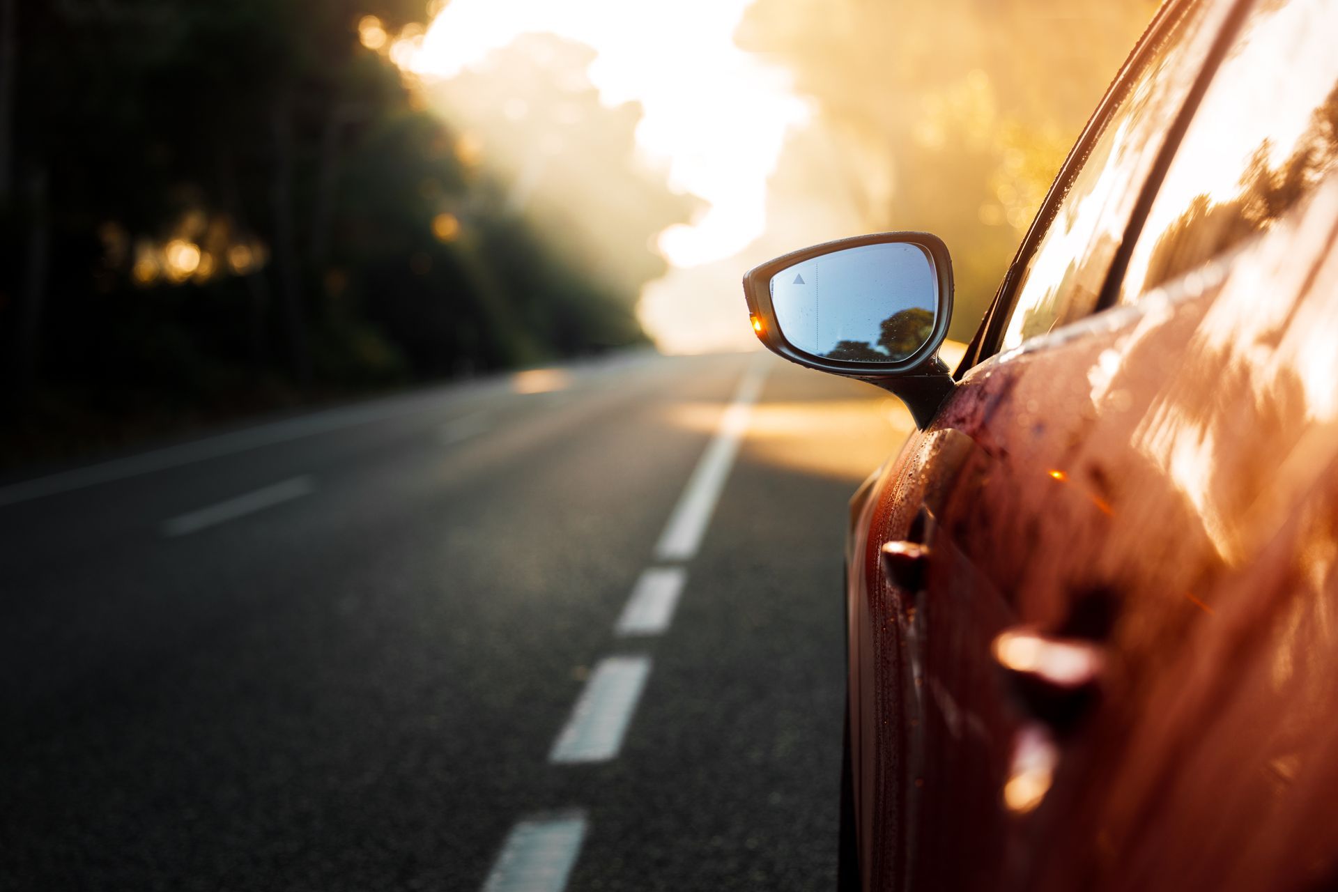 A red car parked on the shoulder of a road during a bright, sunny sunset. | Hunts Point Service Station