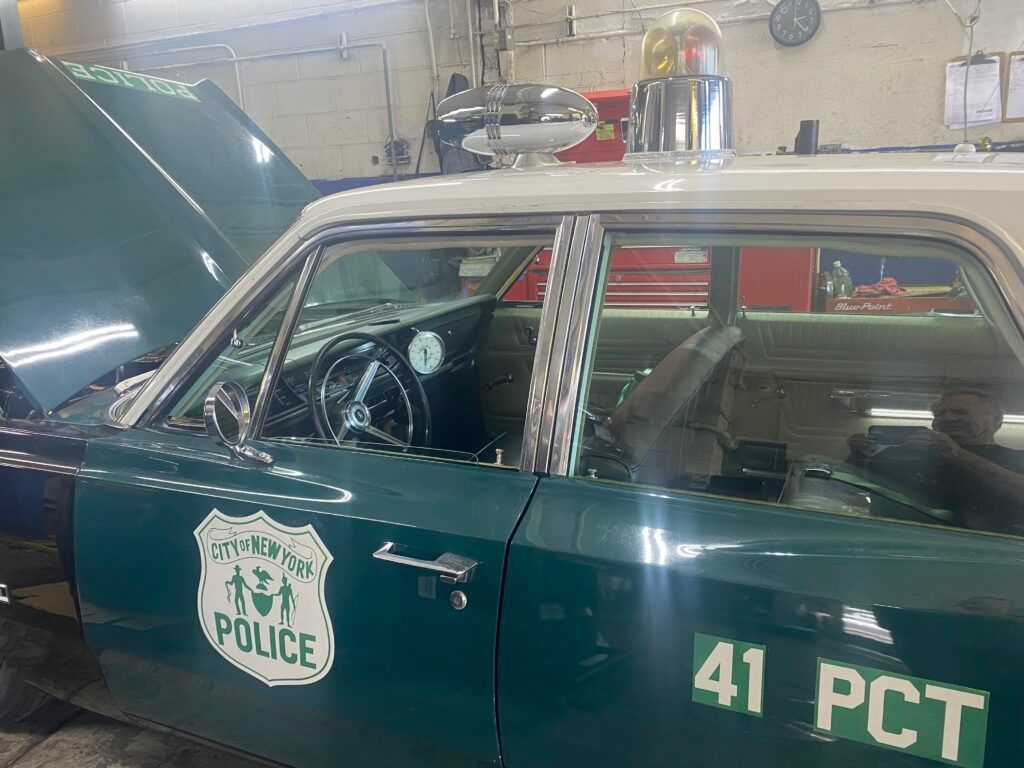 A vintage green and white NYPD police cruiser with an open hood, parked inside a garage. | Hunts Point Service Station