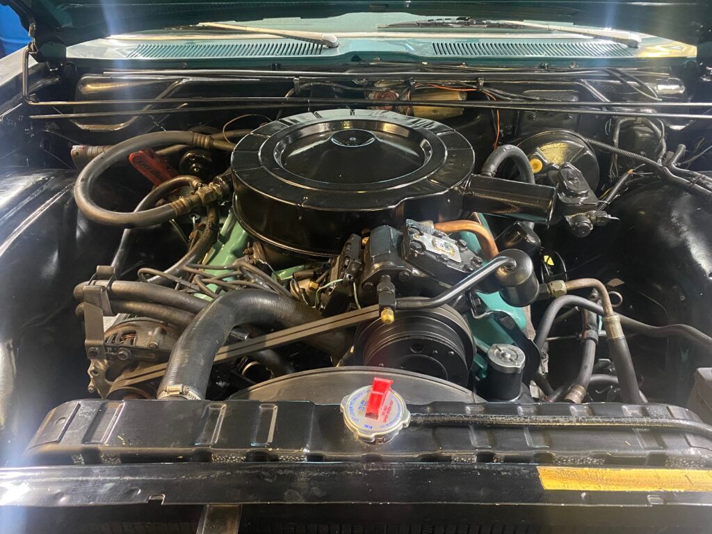 A view inside a car engine bay, showing a black air cleaner assembly mounted on top of a classic green engine. | Hunts Point Service Station