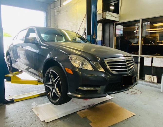 A dark gray Mercedes-Benz sedan raised on a yellow hydraulic automotive lift inside a repair shop. | Hunts Point Service Station