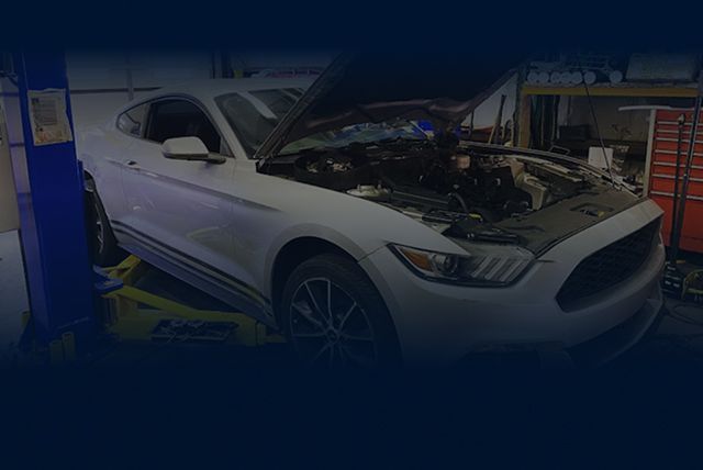 A silver Ford Mustang with its hood open, positioned on a vehicle lift inside an auto repair shop. | Hunts Point Service Station