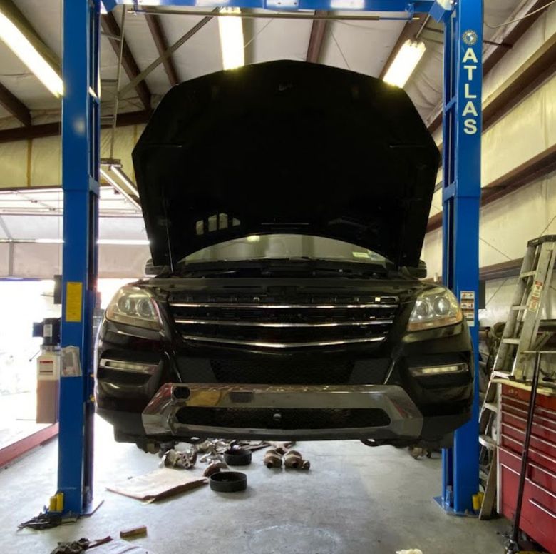 A black SUV with its hood up is raised on a blue hydraulic two-post lift inside an auto repair shop. | Hunts Point Service Station