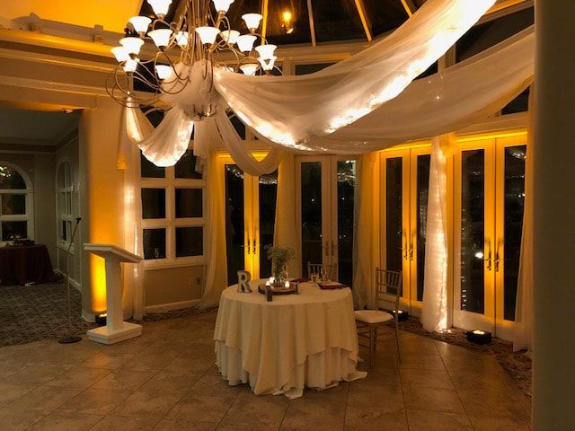 Elegant room lit with gold, draped fabric, a chandelier, and a table set for an event.