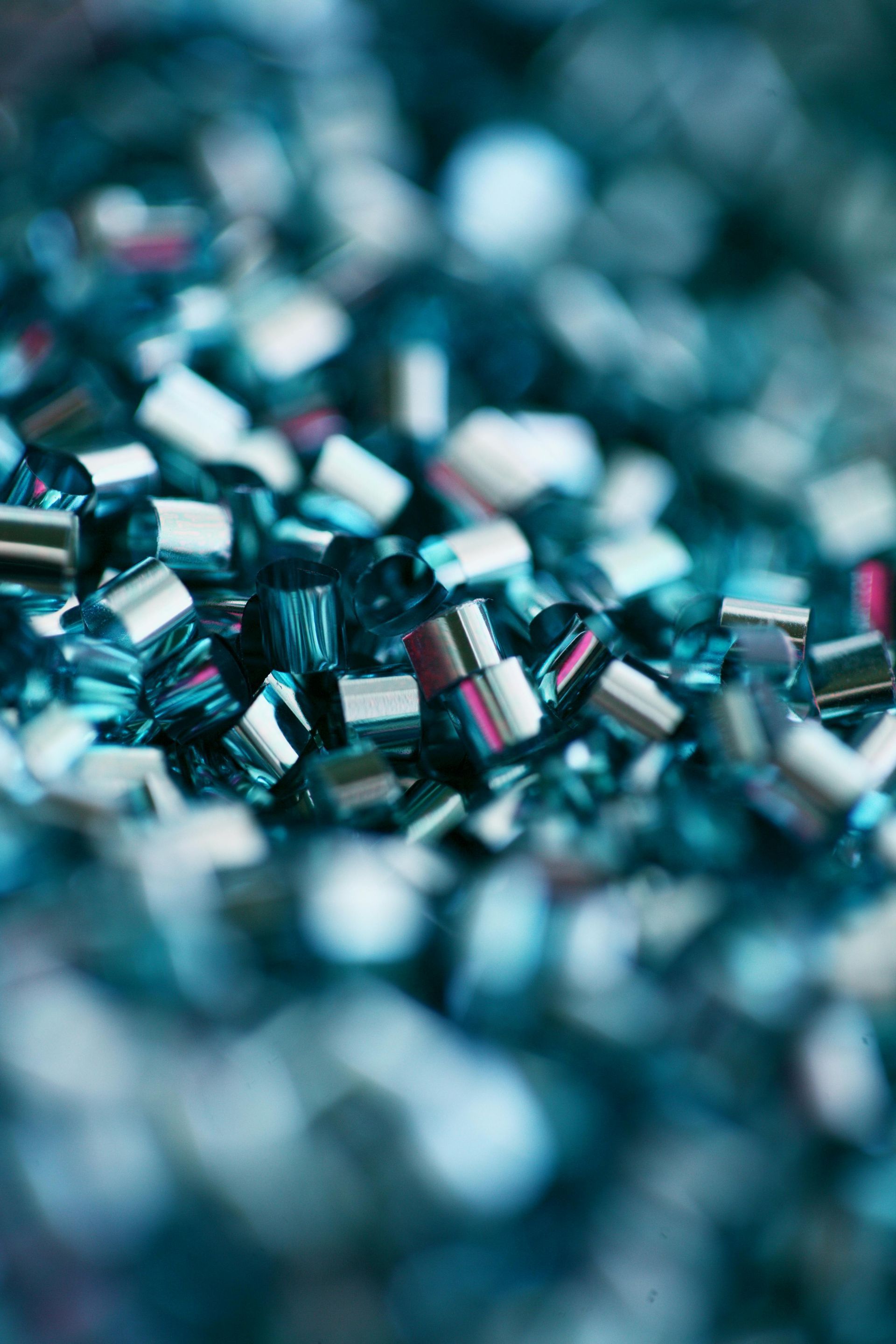 Close-up of a pile of small, blue-green, cylindrical beads with silver ends, creating a sparkling effect.