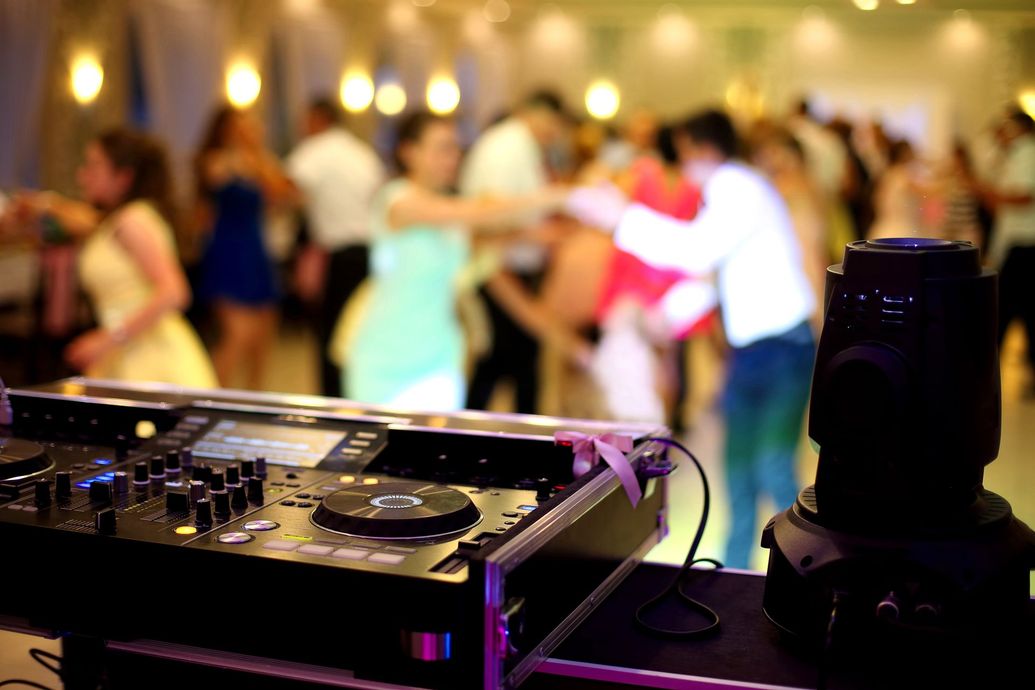 DJ setup in foreground; blurred view of people dancing at a party.