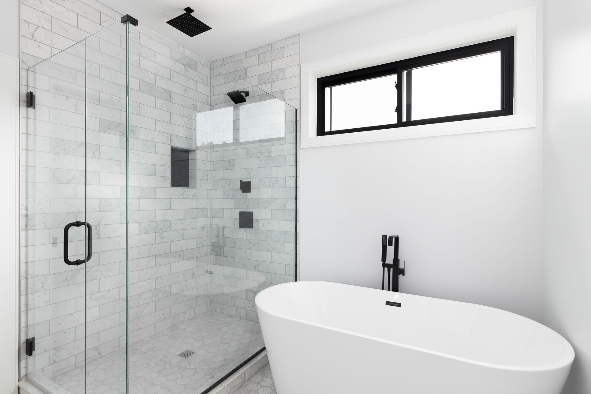 A custom glass shower and freestanding bathtub with marble subway tiles and black features.