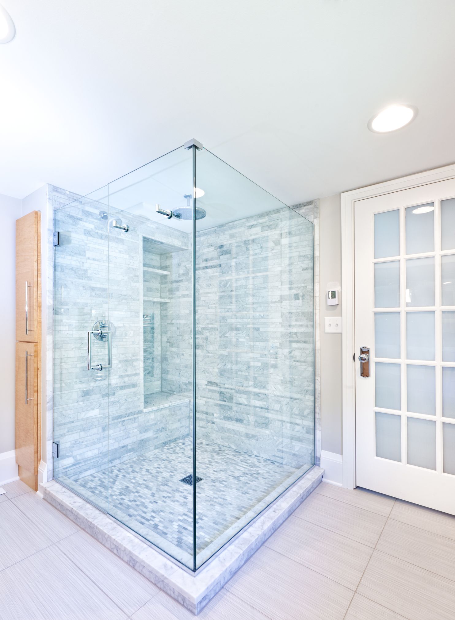 Custom glass showers in modern bathroom with marble tiles and frameless glass shower enclosure.