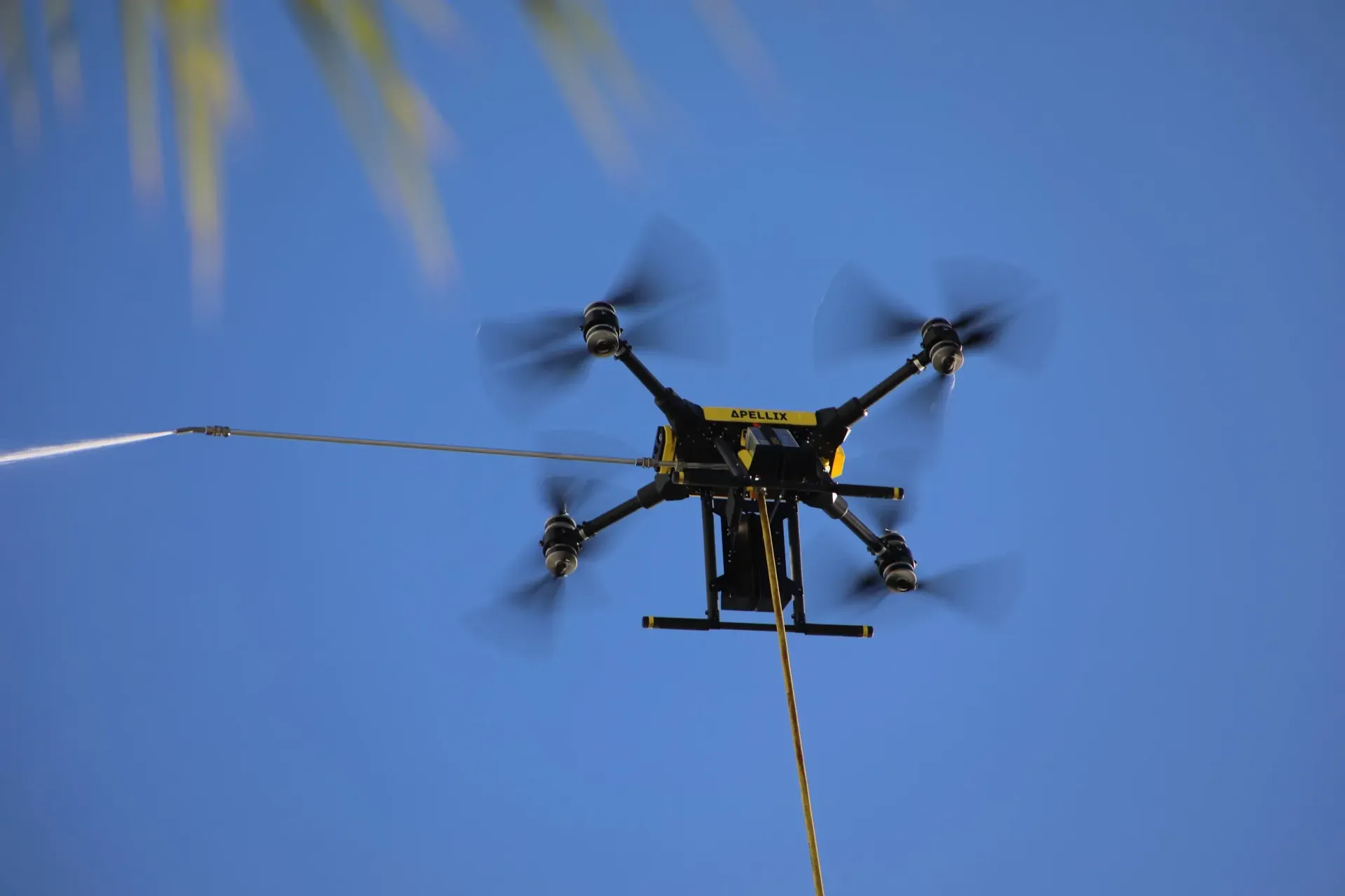 Drone with six rotors flying against a bright blue sky, trailing a line.