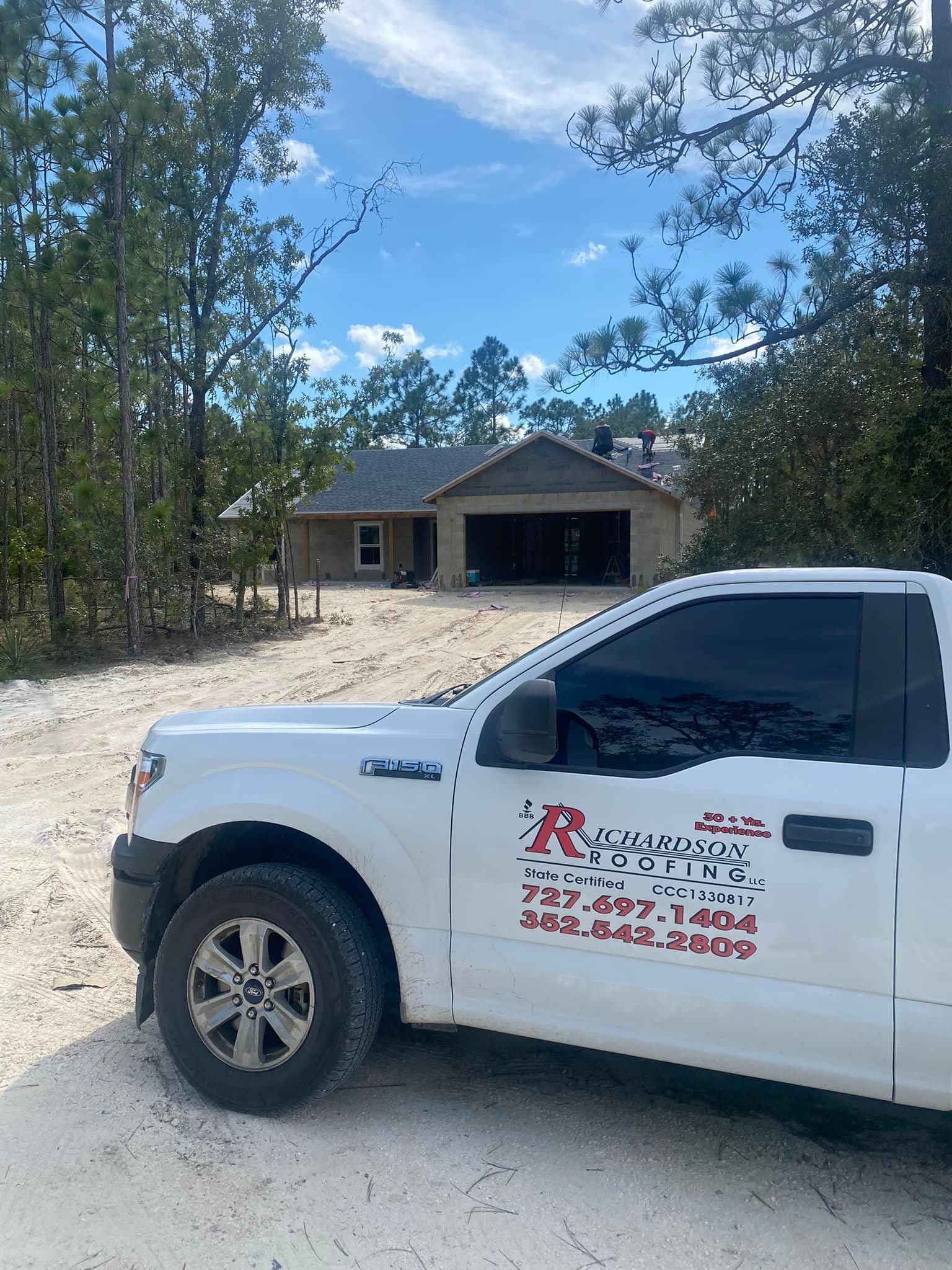 A white truck is parked in front of a house under construction.