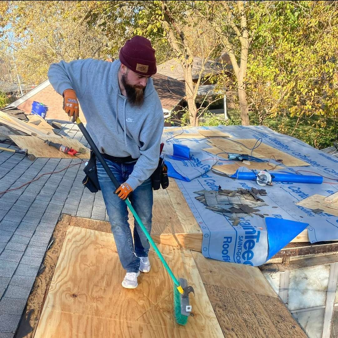 A man is brushing a roof with a green broom