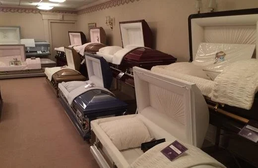 Inside a funeral home showroom, several open and closed coffins on display.