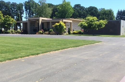 Exterior of a building with a lawn, asphalt road, and trees, likely a crematorium or mausoleum.
