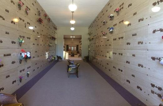 Interior of a columbarium with rows of niches, flowers, and two chairs.