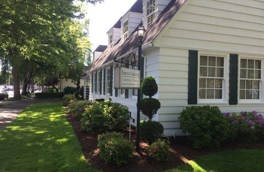 White building with dark green shutters, sign reads 
