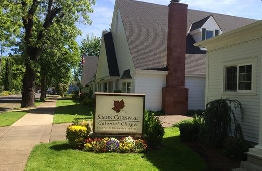 Sign for Smith-Cornwell Colonial Chapel with building in the background. Green lawn, sign with floral bed.