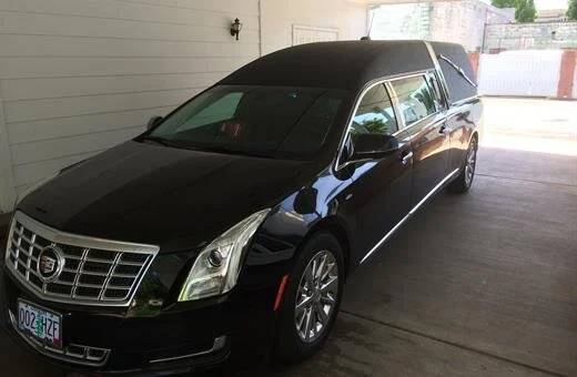 Black Cadillac hearse parked under a white awning.