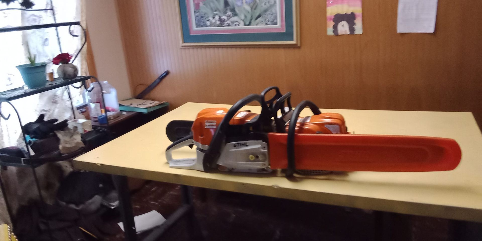 Chainsaw on a yellow table in a room with wood paneling and a window.