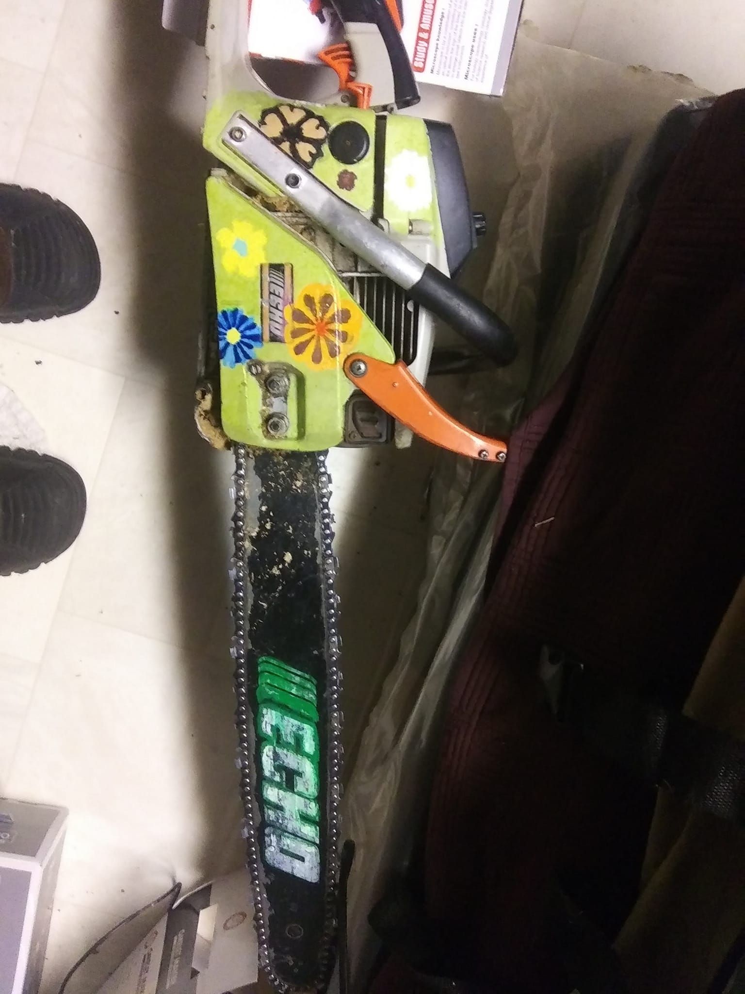 Green and black Echo chainsaw with an orange handle and flower decals, on a light-colored floor.