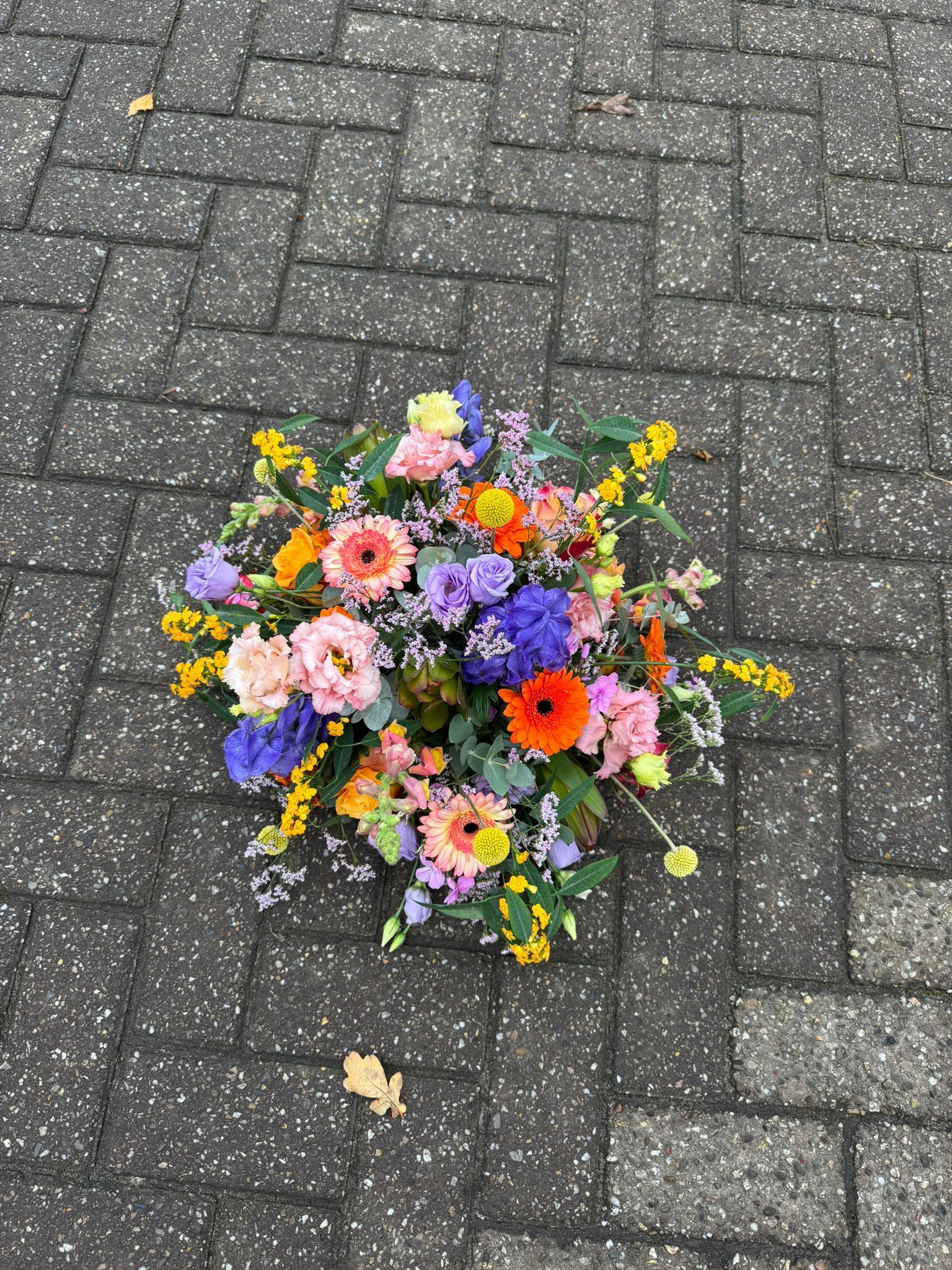 Een levendig, kleurrijk bloemstuk op een donkergrijze, met visgraatpatroon bedekte bakstenen ondergrond.
