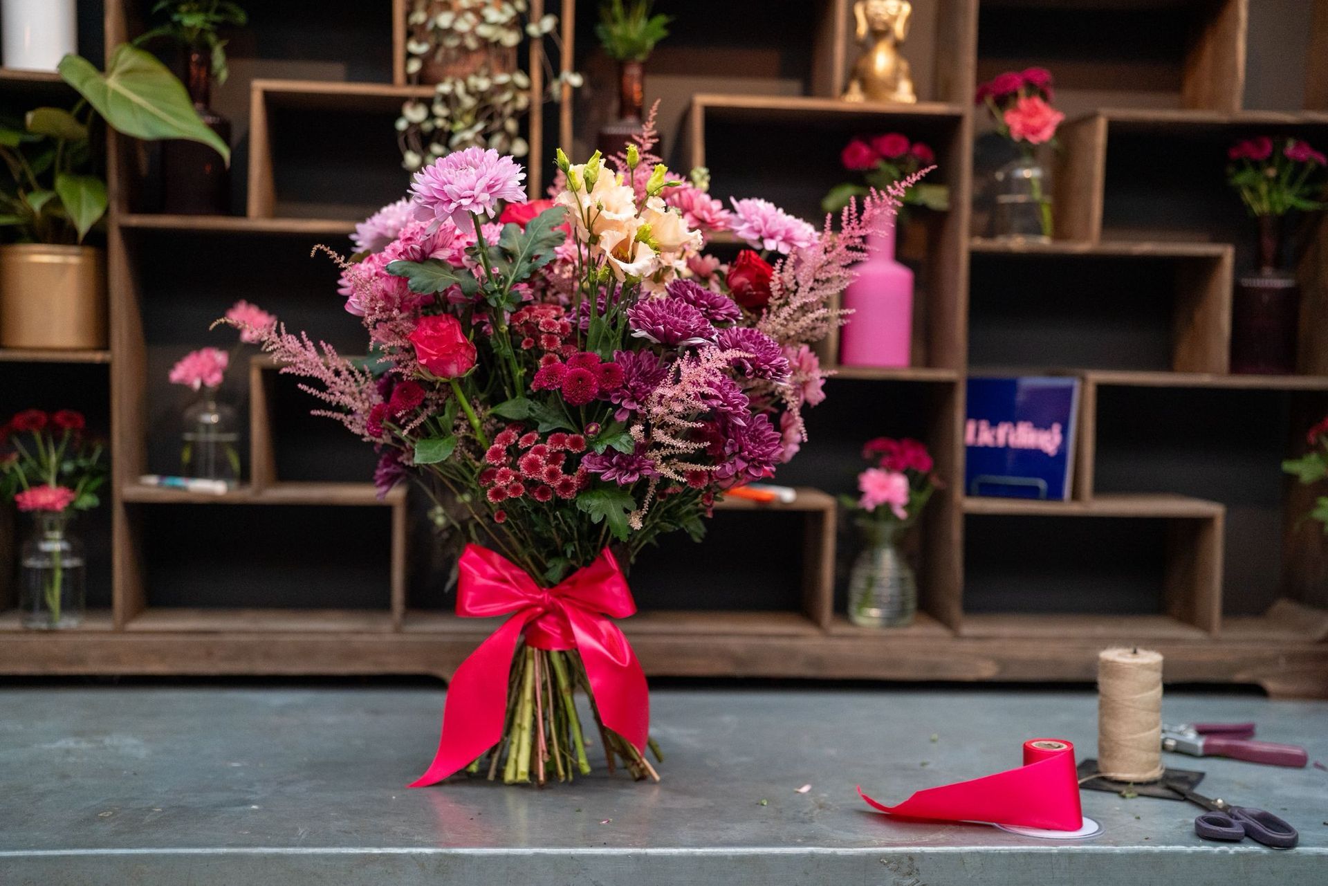 Een levendig boeket roze en paarse bloemen, bijeengebonden met een felroze lint, staat op een tafel voor opbergvakken.