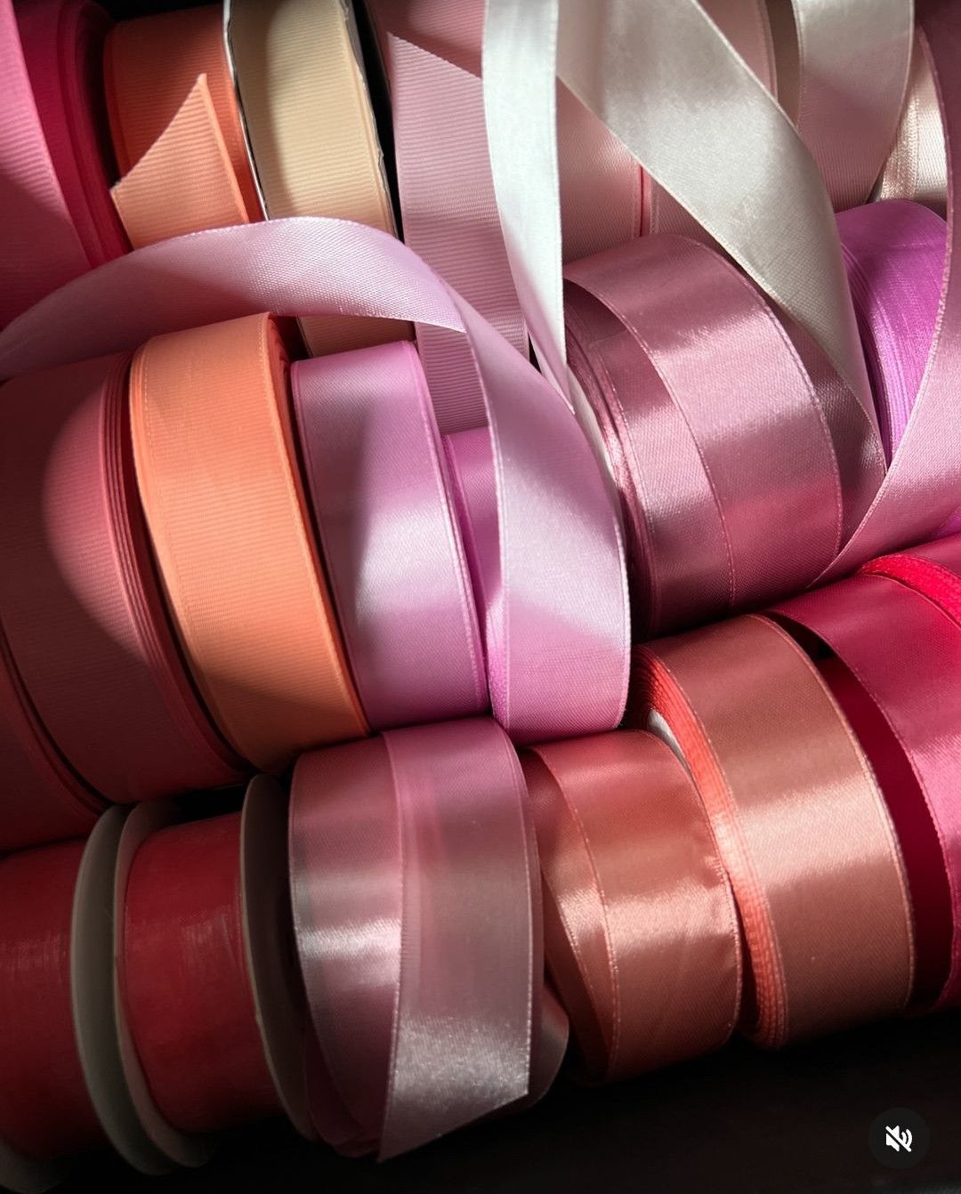 Een verzameling lintrollen in verschillende tinten roze, perzik en wit, dicht bij elkaar gerangschikt.