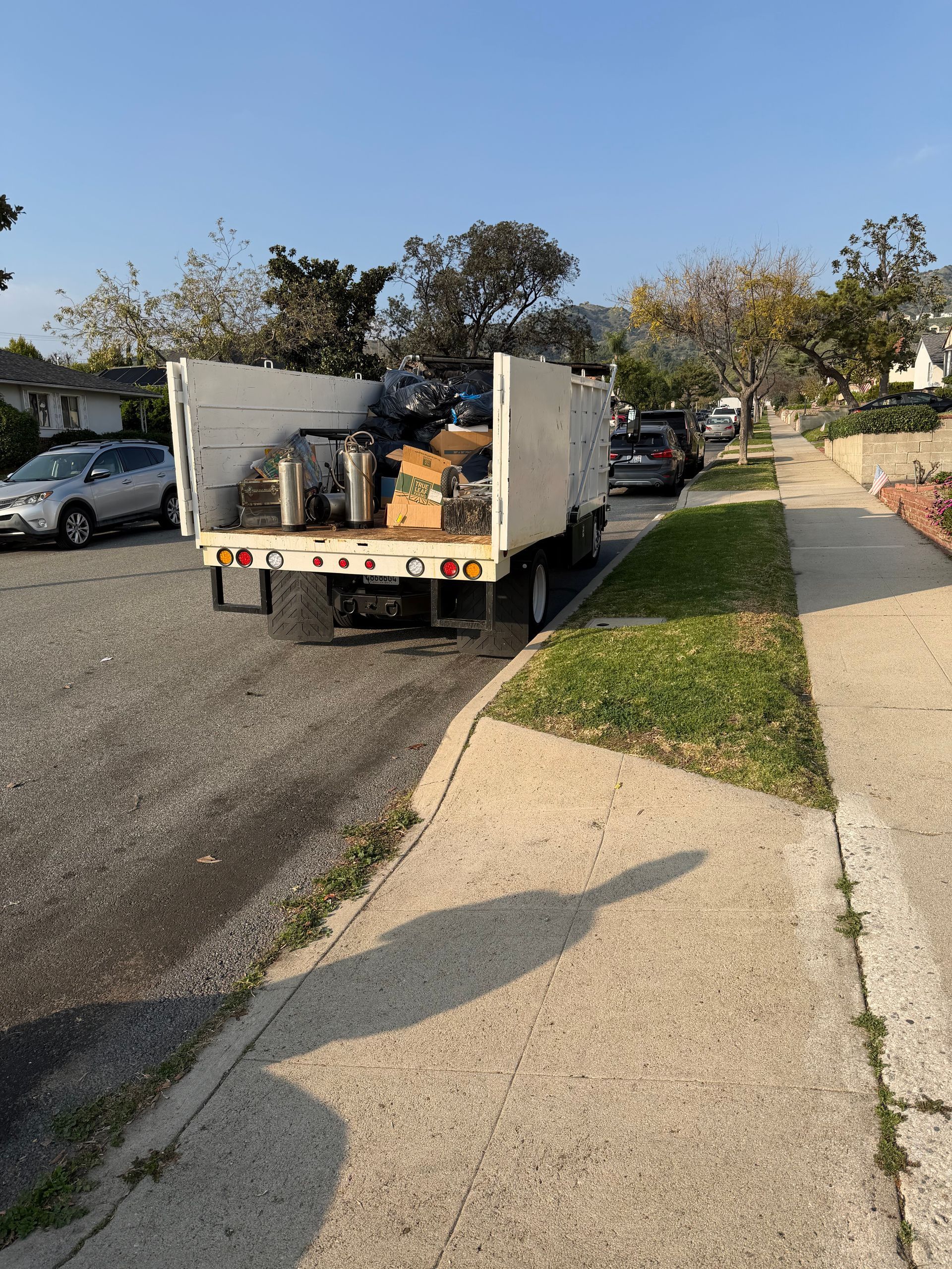 White dump truck filled with debris parked on residential street next to a sidewalk.