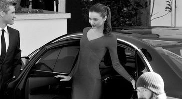 Woman in a dress stepping out of a car while a man in a suit stands nearby.