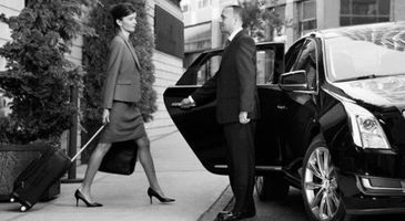 Woman stepping from black car while valet holds the door on a city sidewalk