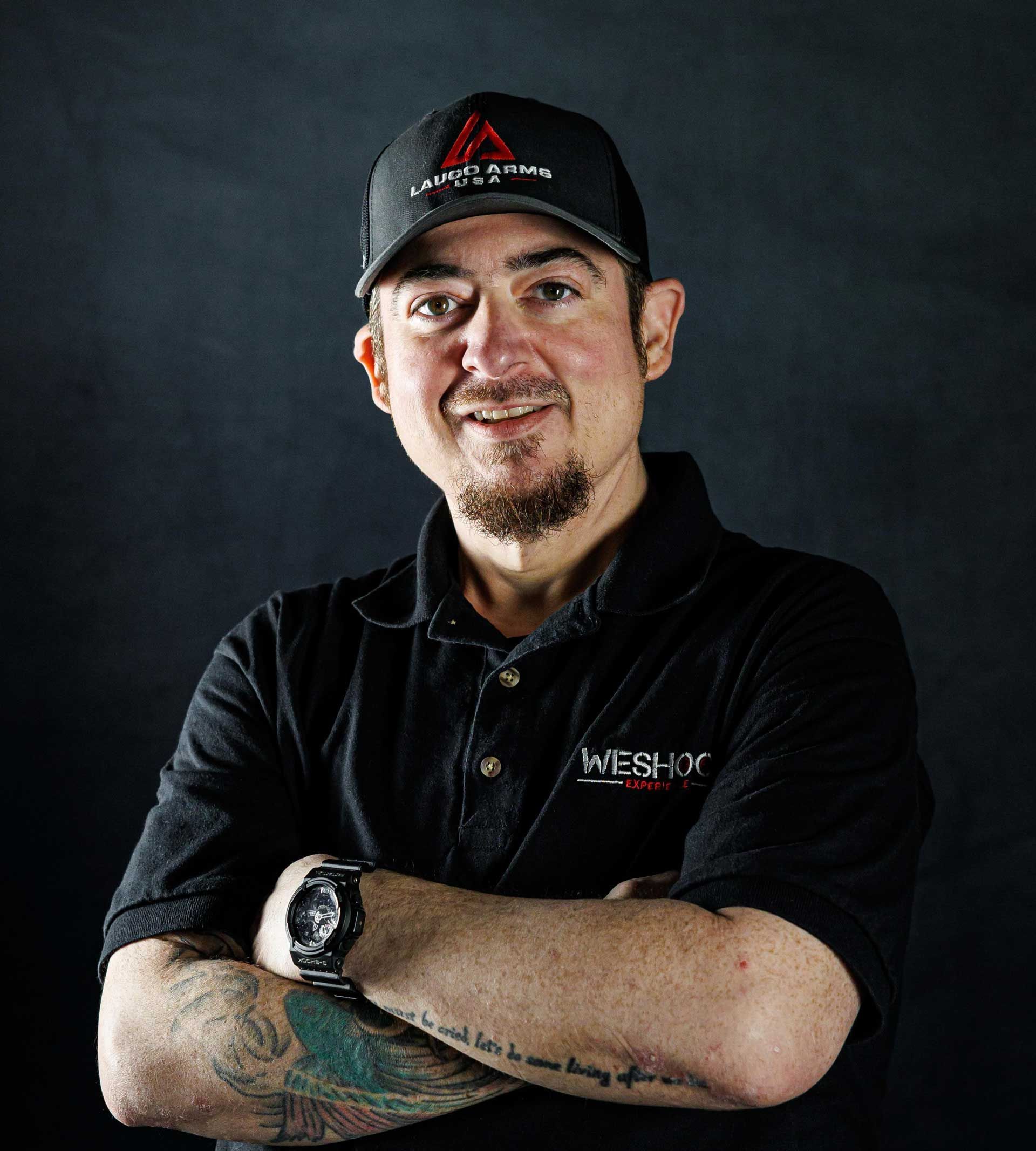 A man wearing a hat and a black shirt is standing with his arms crossed.