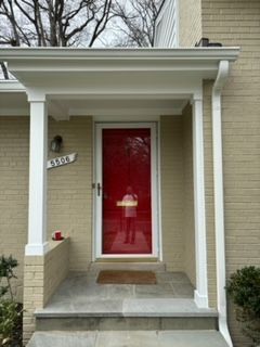 The front door of a house with a red door and a white porch.