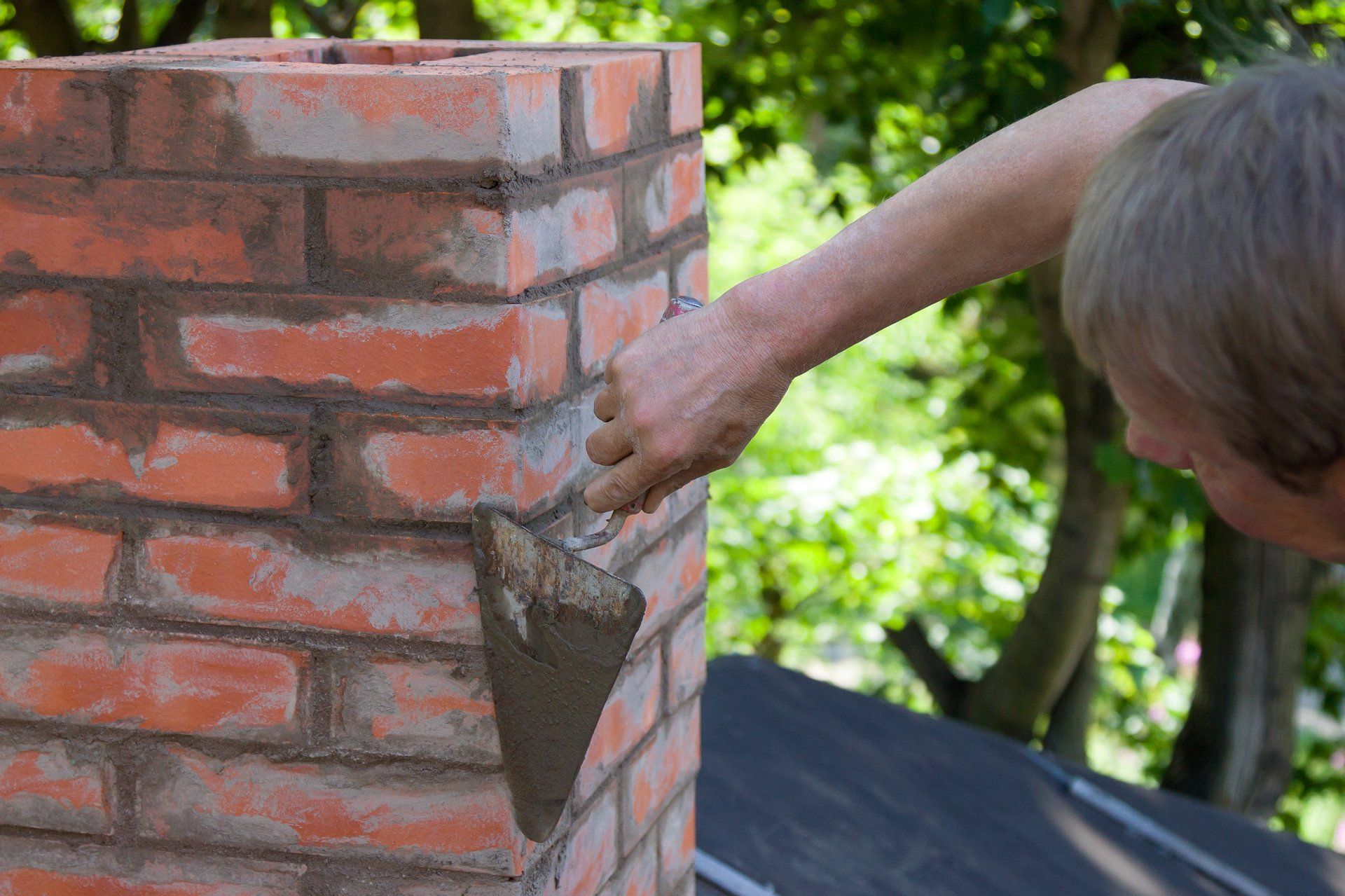A man is using a trowel to apply mortar to a brick chimney.
