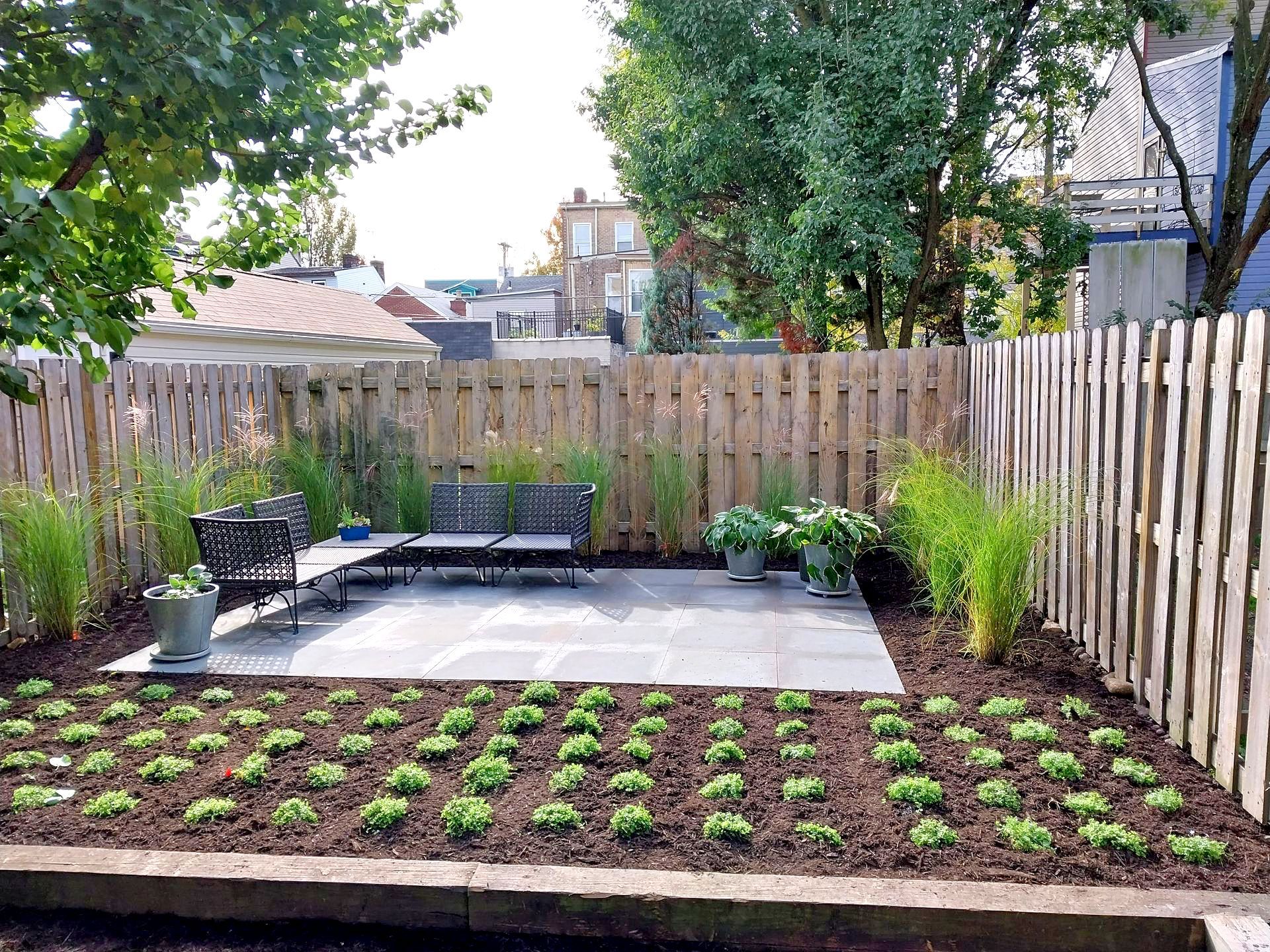 A backyard with a wooden fence and a patio with a bench and chairs.