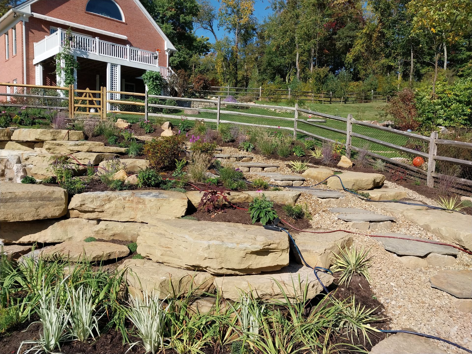A large rock garden with a fence and a house in the background.