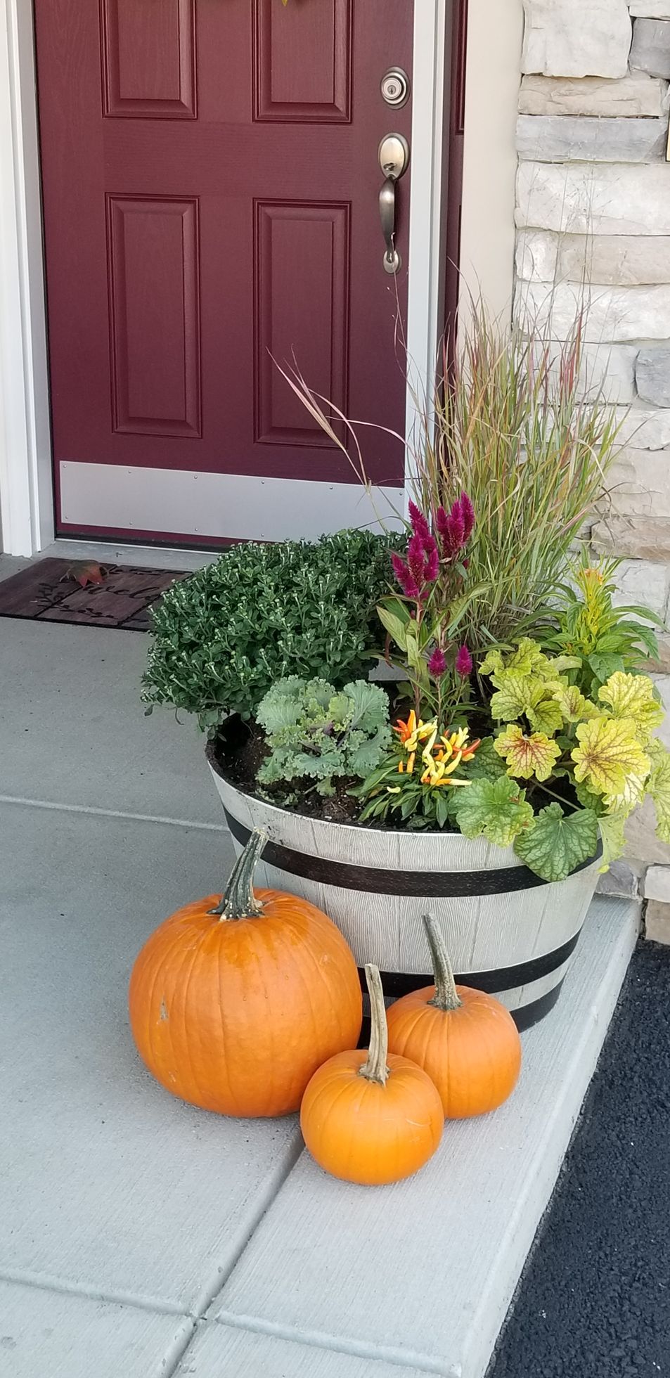 A planter filled with flowers and pumpkins on a porch.
