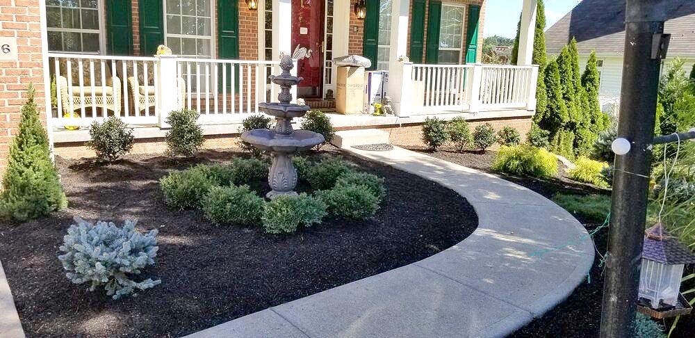 A walkway leading to a house with a fountain in the front yard.
