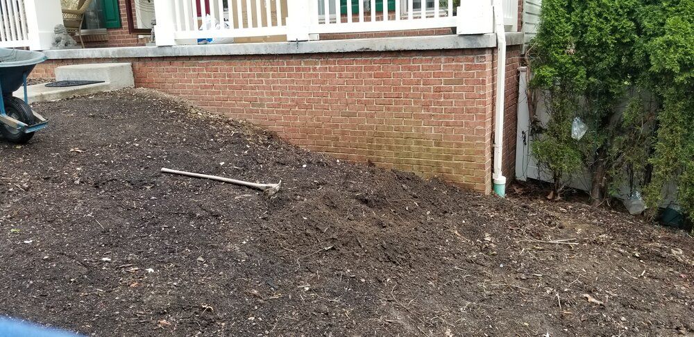A person is raking a pile of mulch in front of a brick house.