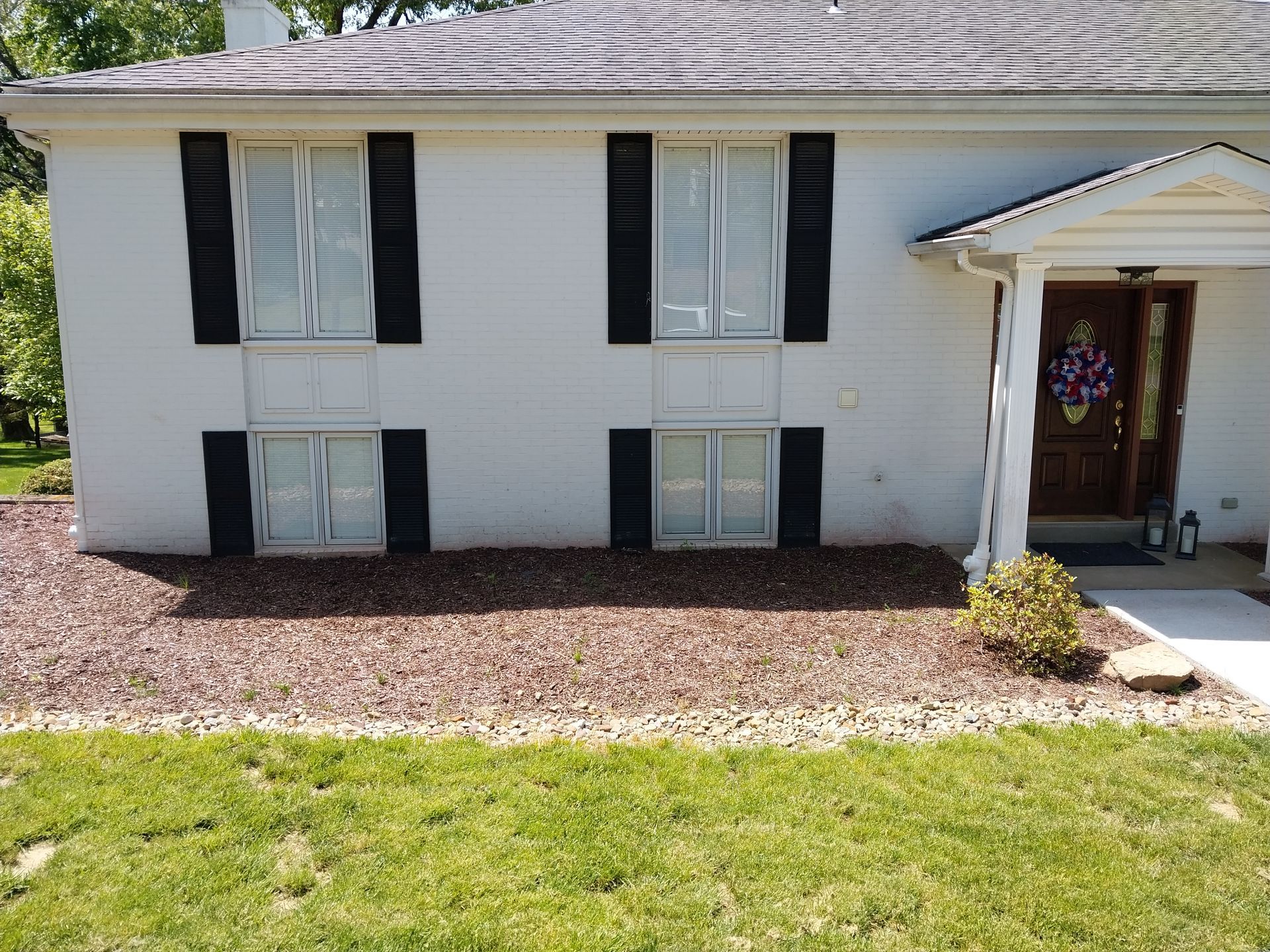 A white house with black shutters is sitting on top of a lush green lawn.