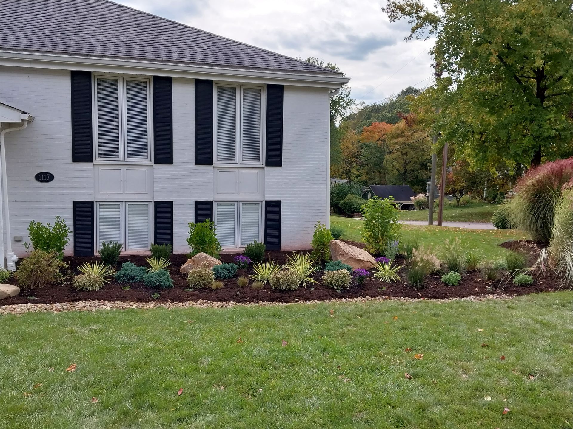 A white house with black shutters and a lush green lawn in front of it.